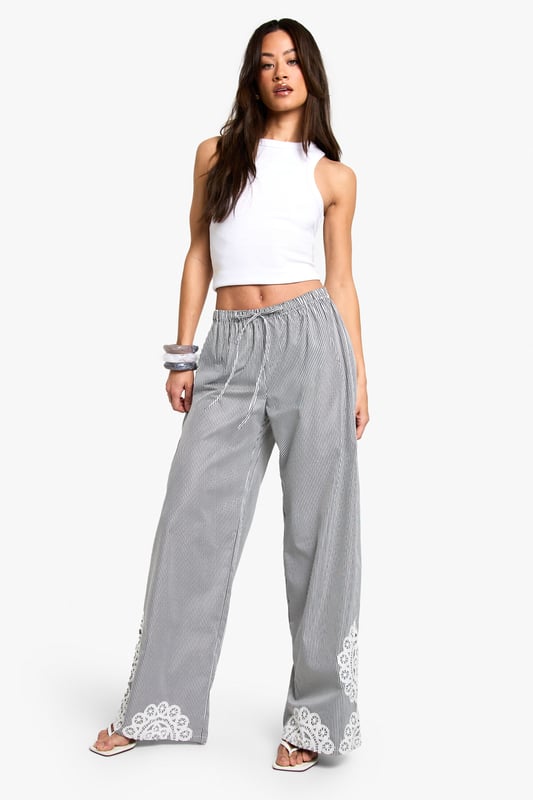 Wide leg trousers featuring delicate floral embroidery detailing at the hem
        Comfortable elasticated waistband with adjustable drawstring tie
        Classic pinstripe pattern throughout for a subtle textured look
        Relaxed, flowing silhouette perfect for taller frames
        Woven fabric that drapes beautifully for effortless movement
    
    These striking wide leg trousers combine casual comfort with distinctive style. The standout floral embroidery at the hem creates a beautiful focal point, while the pinstripe pattern adds a touch of sophistication to your everyday wardrobe. Style with a simple crop top as shown for a balanced silhouette that showcases the dramatic wide leg cut. These trousers are perfect for casual gatherings where you want to make an impression without sacrificing comfort. Pair with flat sandals and a small handbag for daytime events, or dress them up with wedges and statement jewellery for evening occasions. The relaxed fit makes these trousers ideal for family gatherings, brunches with friends, or stylish yet comfortable travel attire. Their versatility allows for countless styling options throughout the seasons.