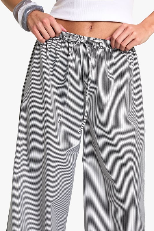 Wide leg trousers featuring delicate floral embroidery detailing at the hem
        Comfortable elasticated waistband with adjustable drawstring tie
        Classic pinstripe pattern throughout for a subtle textured look
        Relaxed, flowing silhouette perfect for taller frames
        Woven fabric that drapes beautifully for effortless movement
    
    These striking wide leg trousers combine casual comfort with distinctive style. The standout floral embroidery at the hem creates a beautiful focal point, while the pinstripe pattern adds a touch of sophistication to your everyday wardrobe. Style with a simple crop top as shown for a balanced silhouette that showcases the dramatic wide leg cut. These trousers are perfect for casual gatherings where you want to make an impression without sacrificing comfort. Pair with flat sandals and a small handbag for daytime events, or dress them up with wedges and statement jewellery for evening occasions. The relaxed fit makes these trousers ideal for family gatherings, brunches with friends, or stylish yet comfortable travel attire. Their versatility allows for countless styling options throughout the seasons.