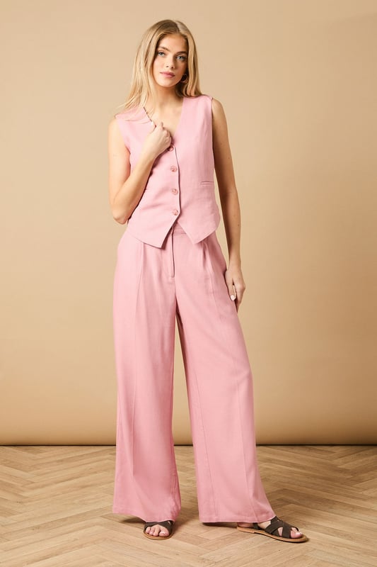 Tailored wide leg design with elegant front pleats for a flattering silhouette
        High-rise waistband with button fastening for a secure and comfortable fit
        Practical side pockets perfect for everyday essentials
        Flowing wide leg cut creates a graceful drape when walking
        Versatile woven fabric suitable for both formal occasions and smart-casual styling
    
    These sophisticated wide leg trousers from Oasis present the perfect balance of comfort and elegance. The tailored design features a flattering high waist that creates a sleek silhouette, whilst the generous wide leg cut offers a contemporary twist on classic formal wear. Style with the coordinating waistcoat for a chic two-piece ensemble perfect for summer weddings and race day events. For more relaxed occasions, pair with a simple silk camisole and metallic sandals as shown. The clean lines and structured fabric make these trousers an excellent choice for important meetings or graduation ceremonies, whilst their lightweight feel ensures you'll remain comfortable throughout the day. Add statement jewellery and a clutch bag to transform them into an evening-ready outfit that radiates refined femininity.
