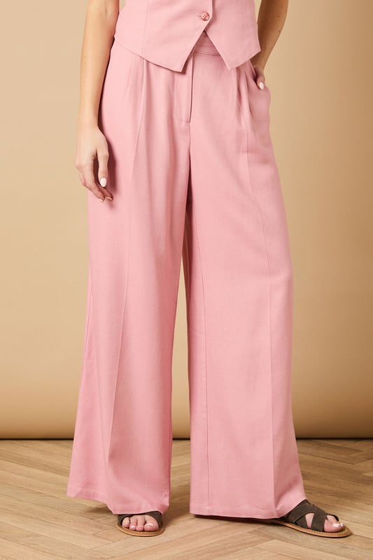 Tailored wide leg design with elegant front pleats for a flattering silhouette
        High-rise waistband with button fastening for a secure and comfortable fit
        Practical side pockets perfect for everyday essentials
        Flowing wide leg cut creates a graceful drape when walking
        Versatile woven fabric suitable for both formal occasions and smart-casual styling
    
    These sophisticated wide leg trousers from Oasis present the perfect balance of comfort and elegance. The tailored design features a flattering high waist that creates a sleek silhouette, whilst the generous wide leg cut offers a contemporary twist on classic formal wear. Style with the coordinating waistcoat for a chic two-piece ensemble perfect for summer weddings and race day events. For more relaxed occasions, pair with a simple silk camisole and metallic sandals as shown. The clean lines and structured fabric make these trousers an excellent choice for important meetings or graduation ceremonies, whilst their lightweight feel ensures you'll remain comfortable throughout the day. Add statement jewellery and a clutch bag to transform them into an evening-ready outfit that radiates refined femininity.