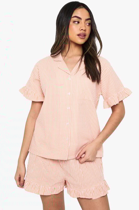 Classic gingham pattern throughout for a timeless nightwear aesthetic
        Charming ruffle detailing on both the short sleeves and shorts hems
        Relaxed button-up shirt with traditional collar for a smart-casual bedtime look
        Comfortable loose-fitting shorts with elasticated waist for ease of movement
        Coordinated two-piece set designed for mix-and-match versatility
    
    Drift into dreamland with this delightful gingham pyjama set from Boohoo. The playful ruffle details add a feminine touch to this classic nightwear ensemble, whilst the relaxed fit ensures maximum comfort for those cosy nights in. The traditional collar and button-up design lend a touch of sophistication to your evening routine. Perfect for lazy Sunday mornings with a cuppa and your favourite book, or for packing on weekend getaways when you want to feel put-together even at bedtime. The coordinated set works brilliantly as a complete look, but can also be paired separately with other nightwear favourites. For cooler evenings, simply layer with a soft dressing gown and fluffy slippers to complete your nighttime ensemble. This charming set embodies Boohoo's commitment to creating fashion that's both fun and functional for the style-conscious night owl.