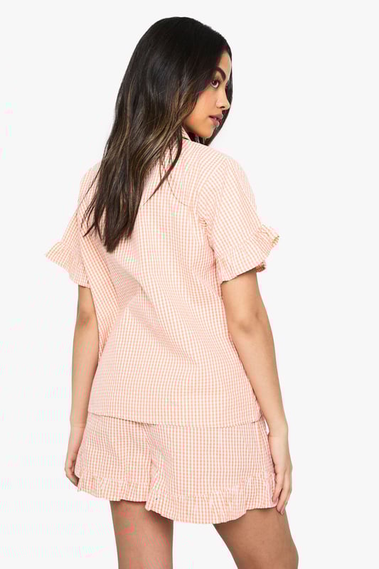 Classic gingham pattern throughout for a timeless nightwear aesthetic
        Charming ruffle detailing on both the short sleeves and shorts hems
        Relaxed button-up shirt with traditional collar for a smart-casual bedtime look
        Comfortable loose-fitting shorts with elasticated waist for ease of movement
        Coordinated two-piece set designed for mix-and-match versatility
    
    Drift into dreamland with this delightful gingham pyjama set from Boohoo. The playful ruffle details add a feminine touch to this classic nightwear ensemble, whilst the relaxed fit ensures maximum comfort for those cosy nights in. The traditional collar and button-up design lend a touch of sophistication to your evening routine. Perfect for lazy Sunday mornings with a cuppa and your favourite book, or for packing on weekend getaways when you want to feel put-together even at bedtime. The coordinated set works brilliantly as a complete look, but can also be paired separately with other nightwear favourites. For cooler evenings, simply layer with a soft dressing gown and fluffy slippers to complete your nighttime ensemble. This charming set embodies Boohoo's commitment to creating fashion that's both fun and functional for the style-conscious night owl.