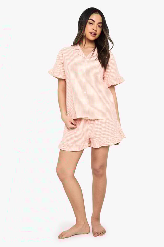Classic gingham pattern throughout for a timeless nightwear aesthetic
        Charming ruffle detailing on both the short sleeves and shorts hems
        Relaxed button-up shirt with traditional collar for a smart-casual bedtime look
        Comfortable loose-fitting shorts with elasticated waist for ease of movement
        Coordinated two-piece set designed for mix-and-match versatility
    
    Drift into dreamland with this delightful gingham pyjama set from Boohoo. The playful ruffle details add a feminine touch to this classic nightwear ensemble, whilst the relaxed fit ensures maximum comfort for those cosy nights in. The traditional collar and button-up design lend a touch of sophistication to your evening routine. Perfect for lazy Sunday mornings with a cuppa and your favourite book, or for packing on weekend getaways when you want to feel put-together even at bedtime. The coordinated set works brilliantly as a complete look, but can also be paired separately with other nightwear favourites. For cooler evenings, simply layer with a soft dressing gown and fluffy slippers to complete your nighttime ensemble. This charming set embodies Boohoo's commitment to creating fashion that's both fun and functional for the style-conscious night owl.