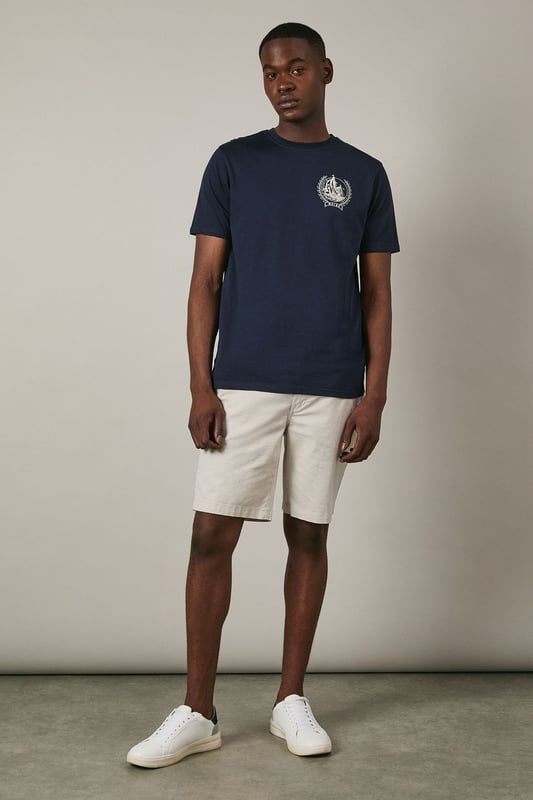 Soft jersey fabric for all-day comfort and breathability
        Classic crew neckline with ribbed trim for a neat finish
        Distinctive coastal ship emblem on chest for nautical appeal
        Short sleeves with clean-cut edges for a streamlined look
        Relaxed fit through the body offering ease of movement
    
    This Maine coastal print t-shirt brings maritime charm to your casual wardrobe. The understated design features a distinctive sailing ship emblem encircled by a laurel wreath, creating a subtle focal point against the navy background. Style it as shown with light-coloured shorts and white trainers for a fresh summer look perfect for beachside strolls or weekend brunches. For cooler evenings, layer under an unstructured blazer or light cotton overshirt. The versatile design transitions effortlessly from daytime casual to relaxed evening gatherings. The cotton jersey construction ensures this t-shirt remains comfortable throughout the day, making it an ideal choice for family outings, casual meet-ups with friends, or simply lounging at home with understated style.