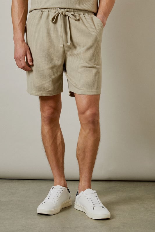 Distinctive seersucker texture adds visual interest and breathability to these casual shorts
        Comfortable elasticated waistband with adjustable drawstring for a personalised fit
        Relaxed leg shape offers ease of movement for all-day comfort
        Mid-thigh length provides a modern silhouette that works for various body types
        Cotton-rich fabric ensures these shorts remain soft and comfortable throughout the day
    
    These Burton seersucker shorts combine classic style with modern comfort, perfect for the man who appreciates timeless fashion. The textured fabric adds subtle sophistication while remaining thoroughly practical for warm-weather wear. Style them as shown with a matching polo shirt for a coordinated look that works brilliantly for weekend barbecues or casual pub gatherings with mates. Alternatively, pair with a crisp white t-shirt and trainers for an effortless daytime ensemble. The neutral tone makes these shorts incredibly versatile, allowing them to complement your existing wardrobe with ease. They're ideal for family gatherings, sporting events, or simply relaxing in the garden on sunny afternoons. Machine washable at 30 degrees, these shorts offer both style and practicality for the modern British man.