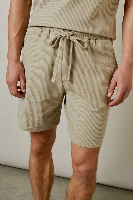 Distinctive seersucker texture adds visual interest and breathability to these casual shorts
        Comfortable elasticated waistband with adjustable drawstring for a personalised fit
        Relaxed leg shape offers ease of movement for all-day comfort
        Mid-thigh length provides a modern silhouette that works for various body types
        Cotton-rich fabric ensures these shorts remain soft and comfortable throughout the day
    
    These Burton seersucker shorts combine classic style with modern comfort, perfect for the man who appreciates timeless fashion. The textured fabric adds subtle sophistication while remaining thoroughly practical for warm-weather wear. Style them as shown with a matching polo shirt for a coordinated look that works brilliantly for weekend barbecues or casual pub gatherings with mates. Alternatively, pair with a crisp white t-shirt and trainers for an effortless daytime ensemble. The neutral tone makes these shorts incredibly versatile, allowing them to complement your existing wardrobe with ease. They're ideal for family gatherings, sporting events, or simply relaxing in the garden on sunny afternoons. Machine washable at 30 degrees, these shorts offer both style and practicality for the modern British man.