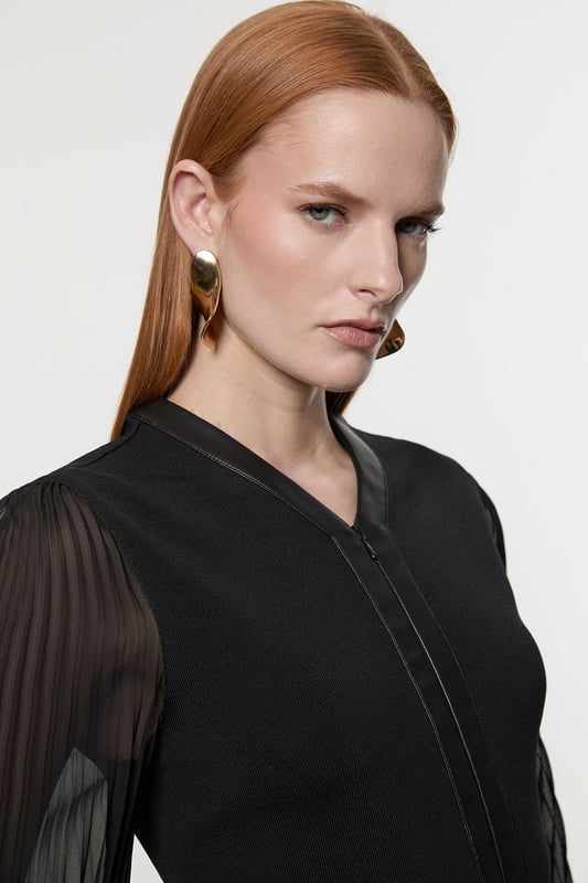 This Karen Millen top seamlessly blends sophistication with contemporary style. The knitted body offers a sleek fit, while the pleated woven sleeves add a touch of drama and movement. The faux leather trim along the V-neckline and waistband creates a striking contrast, enhancing the overall silhouette. Perfect for both day and evening wear, this top can be styled with tailored trousers and heels for a formal event, or paired with a pencil skirt for an office look. The versatility of this piece allows for endless styling possibilities, making it a valuable addition to any wardrobe. Whether you're attending a wedding, a cocktail party, or a business meeting, this top will ensure you look polished and fashion-forward.  Elegant V-neck design with faux leather trim Pleated woven sleeves for added texture Knitted body with a fitted silhouette Faux leather waistband for a defined shape Versatile piece suitable for various occasions