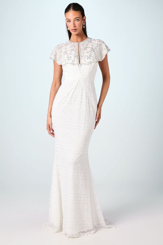 Exquisite hand-stitched cape adorned with sparkling gem embellishments and delicate sequin detailing
        Elegant flutter cap sleeves create a graceful silhouette that frames the shoulders beautifully
        Stunning open back design with sheer panels adds a contemporary touch to this traditional bridal accessory
        Intricate beadwork catches the light with every movement for a truly magical effect
        Versatile piece that can be styled with various wedding gown silhouettes for a personalised bridal look
    
    Make a breathtaking entrance on your special day with this enchanting bridal cape from Coast. The delicate hand-stitched detailing and carefully placed gem embellishments create a halo of radiance around your shoulders, adding a touch of glamour to your wedding ensemble. The thoughtfully designed open back ensures your gown remains the centrepiece whilst the cape adds dimension and visual interest. Style with a sleek updo and drop earrings as seen on our model to showcase the intricate neckline, or wear with flowing locks for a more romantic aesthetic. Perfect for the ceremony and photographs, this cape transitions beautifully from the aisle to the reception, offering a sophisticated layer that can be removed later to reveal a second look for evening celebrations. A truly special accessory that will become a cherished keepsake of your wedding day.