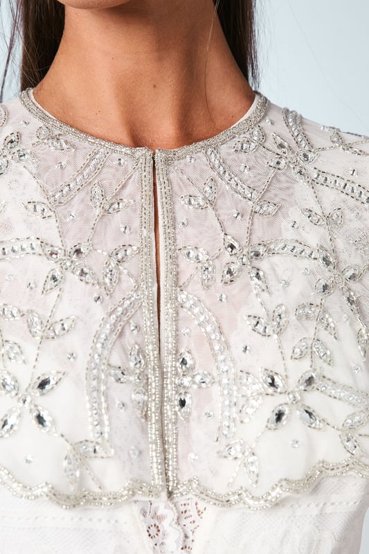 Exquisite hand-stitched cape adorned with sparkling gem embellishments and delicate sequin detailing
        Elegant flutter cap sleeves create a graceful silhouette that frames the shoulders beautifully
        Stunning open back design with sheer panels adds a contemporary touch to this traditional bridal accessory
        Intricate beadwork catches the light with every movement for a truly magical effect
        Versatile piece that can be styled with various wedding gown silhouettes for a personalised bridal look
    
    Make a breathtaking entrance on your special day with this enchanting bridal cape from Coast. The delicate hand-stitched detailing and carefully placed gem embellishments create a halo of radiance around your shoulders, adding a touch of glamour to your wedding ensemble. The thoughtfully designed open back ensures your gown remains the centrepiece whilst the cape adds dimension and visual interest. Style with a sleek updo and drop earrings as seen on our model to showcase the intricate neckline, or wear with flowing locks for a more romantic aesthetic. Perfect for the ceremony and photographs, this cape transitions beautifully from the aisle to the reception, offering a sophisticated layer that can be removed later to reveal a second look for evening celebrations. A truly special accessory that will become a cherished keepsake of your wedding day.