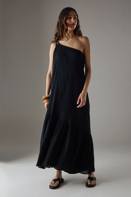Asymmetric one-shoulder design with elegant double strap detail
        Lightweight cheesecloth fabric creates a breezy, effortless drape
        Flowing maxi length with feminine tiered hem detail
        Relaxed silhouette offers comfortable movement for all-day wear
        Versatile sundress that transitions seamlessly from day to evening occasions
    
    This striking Warehouse maxi sundress commands attention with its distinctive asymmetric neckline and double strap detail. The lightweight cheesecloth fabric creates a beautifully fluid silhouette that moves gracefully with every step, while the tiered hem adds a touch of feminine flair. For formal occasions, style with metallic strappy heels and statement gold jewellery as seen on our model - the chunky bangle creates a perfect contrast against the dress's soft texture. Alternatively, embrace a more relaxed daytime look with leather sandals and a woven clutch. The versatile design makes it an ideal choice for summer weddings, garden parties, or sophisticated evening events where you wish to project confidence with an edgy yet feminine aesthetic. The one-shoulder design offers a contemporary twist on classic occasion wear, ensuring you stand out for all the right reasons.