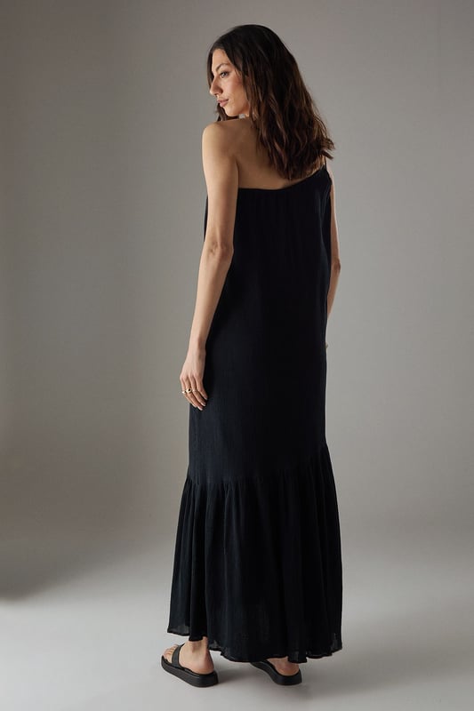 Asymmetric one-shoulder design with elegant double strap detail
        Lightweight cheesecloth fabric creates a breezy, effortless drape
        Flowing maxi length with feminine tiered hem detail
        Relaxed silhouette offers comfortable movement for all-day wear
        Versatile sundress that transitions seamlessly from day to evening occasions
    
    This striking Warehouse maxi sundress commands attention with its distinctive asymmetric neckline and double strap detail. The lightweight cheesecloth fabric creates a beautifully fluid silhouette that moves gracefully with every step, while the tiered hem adds a touch of feminine flair. For formal occasions, style with metallic strappy heels and statement gold jewellery as seen on our model - the chunky bangle creates a perfect contrast against the dress's soft texture. Alternatively, embrace a more relaxed daytime look with leather sandals and a woven clutch. The versatile design makes it an ideal choice for summer weddings, garden parties, or sophisticated evening events where you wish to project confidence with an edgy yet feminine aesthetic. The one-shoulder design offers a contemporary twist on classic occasion wear, ensuring you stand out for all the right reasons.