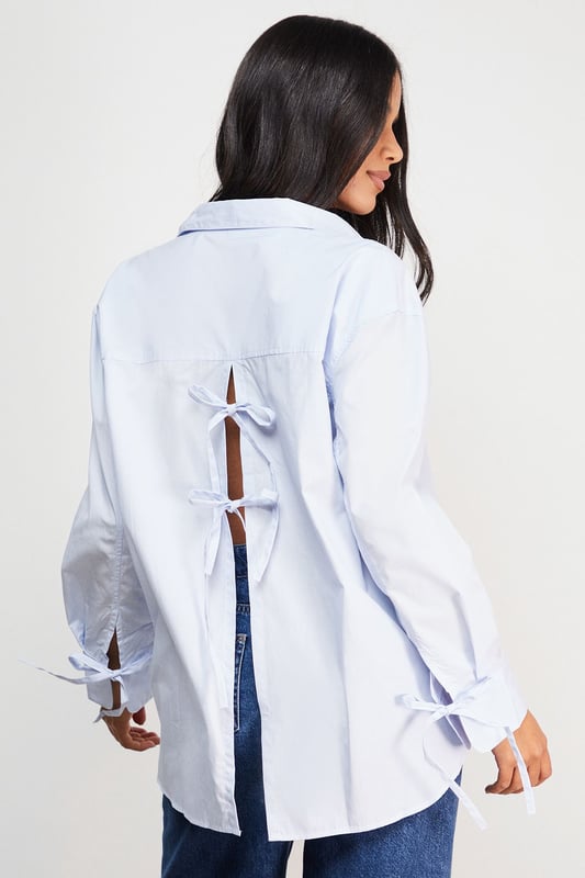 Oversized fit with classic collar and button-through front for a relaxed silhouette
        Distinctive bow-tie back detail creates a feminine twist on the traditional shirt
        Long sleeves with button cuffs offer versatility for year-round styling
        Cotton fabric provides breathable comfort for all-day wear
        Subtle split back design adds movement and contemporary flair
    
    This Warehouse oversized shirt reinvents the classic button-down with its striking bow-back detail. The relaxed fit creates an effortlessly chic look that works beautifully with straight-leg jeans and flats for casual outings. For a more polished ensemble, try half-tucking the front into high-waisted trousers and adding a structured tote. The cotton construction ensures comfort whilst maintaining a crisp appearance throughout the day. Perfect for family gatherings or weekend brunches, this versatile piece transitions seamlessly from daytime casual to evening drinks when paired with statement earrings and ankle boots. The thoughtful back detail adds interest when layered under jumpers or jackets, making this shirt a standout addition to your wardrobe that works across multiple seasons.