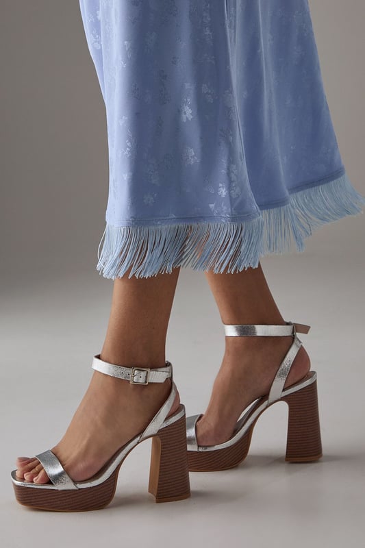 Striking metallic faux leather finish that catches the light beautifully
        Chunky wooden-effect platform for added height and stability
        Elegant high block heel measuring between 7-9cm
        Secure ankle strap with adjustable buckle fastening
        Open toe design perfect for showcasing your favourite pedicure
    
    These Faith Ebony platform sandals combine retro-inspired design with contemporary flair. The metallic finish adds a touch of glamour to any outfit, while the substantial platform and block heel provide comfort without sacrificing style. Pair with flowing midi dresses for garden parties, or team with cropped jeans and an oversized shirt for casual weekend brunches. The ankle strap ensures security while walking, making these an ideal choice for all-day wear despite their impressive height. The versatile design transitions effortlessly from daytime family gatherings to evening drinks with friends. The contrast between the sleek upper and textured wooden-effect heel creates visual interest that will complement both casual and smart-casual ensembles in your wardrobe.