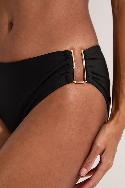 These sophisticated Karen Millen bikini bottoms bring a touch of luxury to your beachwear collection. The striking gold trim adds a refined accent that catches the light beautifully as you lounge poolside or stroll along the shore. Pair with the coordinating bandeau top for a cohesive look that's perfect for your summer getaway. Style with oversized sunglasses and a flowing kaftan for elegant poolside glamour, or team with a linen shirt and sandals when heading to a beachside lunch. These bottoms offer the perfect balance of comfort and sophistication for your next sun-soaked holiday.   Distinctive gold-tone trim detail on the side Mid-rise design offering comfortable coverage and a flattering silhouette Soft, stretchy fabric Sleek, minimalist design that pairs beautifully with the matching bandeau top  Matching piece sold separately.