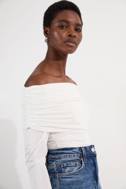 This Karen Millen Bardot bodysuit offers effortless sophistication for your everyday wardrobe. The off-shoulder design creates a flattering silhouette while the slinky jersey fabric drapes across the dcolletage. Style with high-waisted wide-leg jeans, or pair with a flowing midi skirt and ballet flats. For cooler evenings, layer with an oversized cardigan without compromising on the elegant neckline. The versatile design transitions seamlessly from daytime casual to evening drinks, simply swap to block heels and add statement earrings to transform your look.   Elegant Bardot neckline with a ruched fold-over detail Crafted from soft, drapey slinky jersey Secure bodysuit design Long sleeves