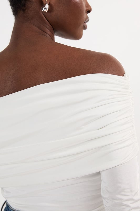 This Karen Millen Bardot bodysuit offers effortless sophistication for your everyday wardrobe. The off-shoulder design creates a flattering silhouette while the slinky jersey fabric drapes across the dcolletage. Style with high-waisted wide-leg jeans, or pair with a flowing midi skirt and ballet flats. For cooler evenings, layer with an oversized cardigan without compromising on the elegant neckline. The versatile design transitions seamlessly from daytime casual to evening drinks, simply swap to block heels and add statement earrings to transform your look.   Elegant Bardot neckline with a ruched fold-over detail Crafted from soft, drapey slinky jersey Secure bodysuit design Long sleeves