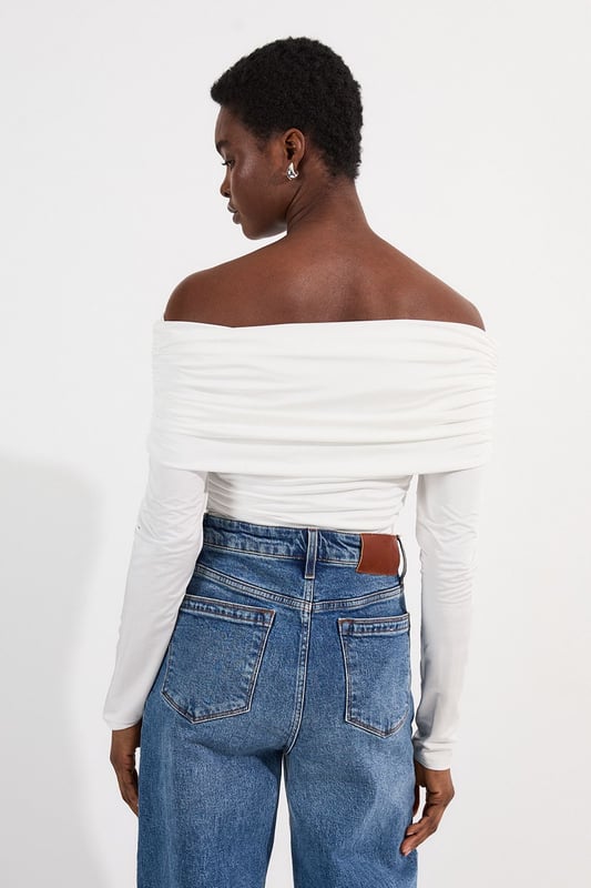 This Karen Millen Bardot bodysuit offers effortless sophistication for your everyday wardrobe. The off-shoulder design creates a flattering silhouette while the slinky jersey fabric drapes across the dcolletage. Style with high-waisted wide-leg jeans, or pair with a flowing midi skirt and ballet flats. For cooler evenings, layer with an oversized cardigan without compromising on the elegant neckline. The versatile design transitions seamlessly from daytime casual to evening drinks, simply swap to block heels and add statement earrings to transform your look.   Elegant Bardot neckline with a ruched fold-over detail Crafted from soft, drapey slinky jersey Secure bodysuit design Long sleeves