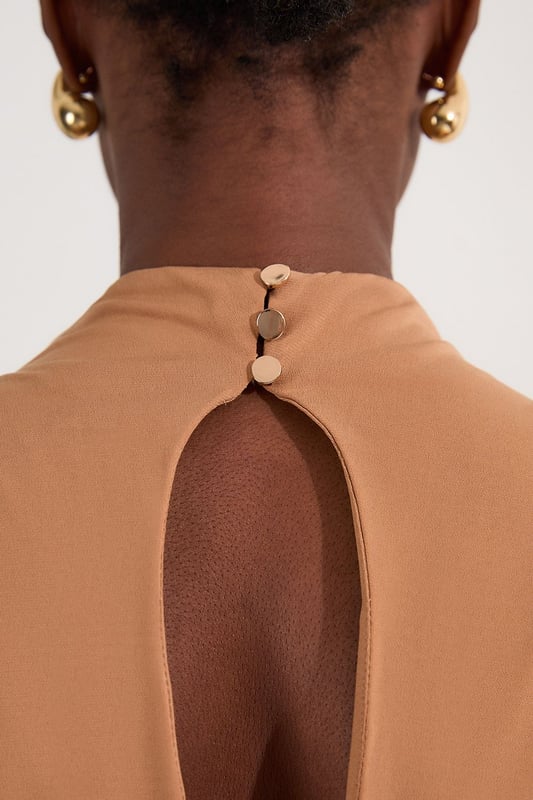 This versatile Karen Millen bodysuit combines contemporary design with everyday wearability. The high neck and artful ruching create a refined silhouette that works beautifully with both casual and smart-casual ensembles. Style with high-waisted trousers as shown for a polished daytime look, perfect for brunches or gallery visits. The sleek design pairs wonderfully with wide-leg jeans and trainers for weekend outings, or dress it up with a tailored blazer and statement jewellery for dinner dates. The bodysuit format eliminates the need for constant readjustment, making it an ideal foundation piece for busy days when comfort and style must work in harmony. Add a leather jacket and ankle boots to transition this piece effortlessly into evening drinks with friends.  Elegant high neck design with sophisticated ruched detailing for a flattering silhouette Sleeveless cut with gentle draping across the bodice for effortless style Bodysuit construction ensures a smooth, tucked-in finish that stays in place all day Soft jersey crepe fabric offers comfortable stretch and movement Stylish back opening with button fastening adds an unexpected design element