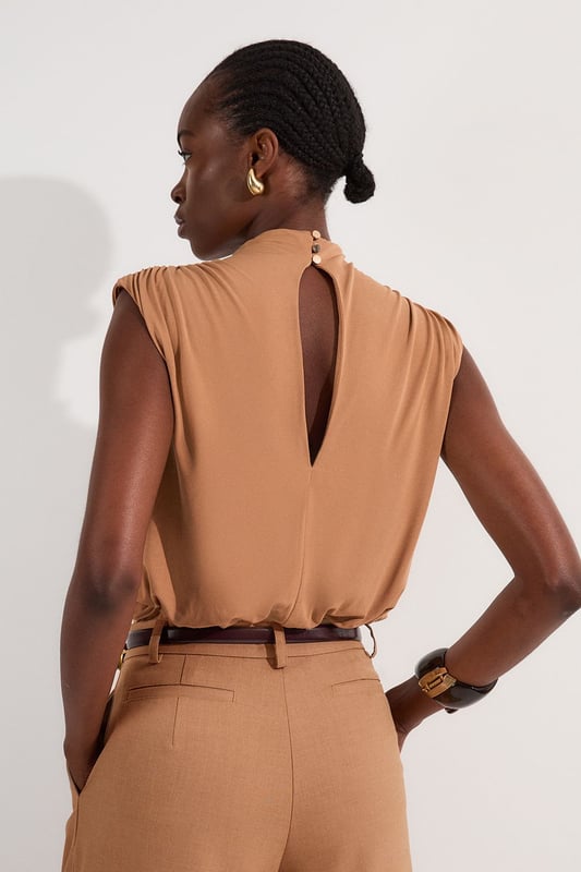 This versatile Karen Millen bodysuit combines contemporary design with everyday wearability. The high neck and artful ruching create a refined silhouette that works beautifully with both casual and smart-casual ensembles. Style with high-waisted trousers as shown for a polished daytime look, perfect for brunches or gallery visits. The sleek design pairs wonderfully with wide-leg jeans and trainers for weekend outings, or dress it up with a tailored blazer and statement jewellery for dinner dates. The bodysuit format eliminates the need for constant readjustment, making it an ideal foundation piece for busy days when comfort and style must work in harmony. Add a leather jacket and ankle boots to transition this piece effortlessly into evening drinks with friends.  Elegant high neck design with sophisticated ruched detailing for a flattering silhouette Sleeveless cut with gentle draping across the bodice for effortless style Bodysuit construction ensures a smooth, tucked-in finish that stays in place all day Soft jersey crepe fabric offers comfortable stretch and movement Stylish back opening with button fastening adds an unexpected design element