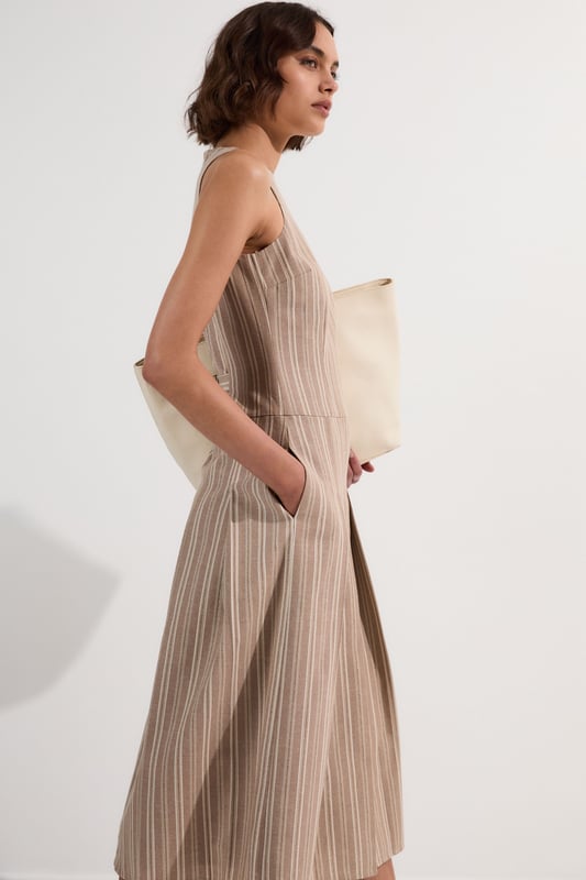This Karen Millen tailored midi dress combines timeless stripes with contemporary design for versatile daywear. The structured bodice flows into a beautifully pleated full skirt, creating a feminine silhouette that's both comfortable and sophisticated. Style with flat leather sandals as shown for casual family gatherings or weekend brunches. For garden parties, pair with espadrille wedges and a woven clutch. The cotton-linen blend fabric offers breathability and a natural texture perfect for warmer months. This dress transitions effortlessly from day to evening, simply swap your casual footwear for block heels and add delicate gold jewellery to complement the dress's hardware detailing. A lightweight cardigan makes this piece suitable for cooler summer evenings.  Sleeveless midi dress with elegant vertical stripe pattern Sophisticated V-neckline for a flattering silhouette Full skirt design with structured pleating for graceful movement Tailored fit through bodice with defined waistline Decorative gold-tone buckle detail adds a refined finishing touch