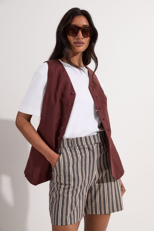 These Karen Millen tailored city shorts combine sophistication with casual comfort for effortless daywear styling. The distinctive stripe pattern with subtle sparkle threads creates visual interest while maintaining versatility. Style them with a crisp white t-shirt and an oversized blazer for a polished weekend brunch look, or pair with a lightweight knit and trainers for shopping trips and casual gatherings. The structured silhouette and linen blend fabric make these shorts perfect for warm-weather socialising without compromising on style. For a coordinated summer ensemble, match with flat sandals and a crossbody bag, adding sunglasses for a touch of chic practicality. These shorts transition seamlessly from daytime family gatherings to early evening garden parties, offering both comfort and refined style.  Tailored city shorts featuring a distinctive sparkle stripe pattern for a touch of subtle glamour Crafted with linen blend fabric for breathable comfort during warm weather Elegant gold-tone buckle detail at the waistband adds a refined finishing touch Practical side pockets for convenient storage of small essentials Versatile 45cm length offering a flattering fit that pairs beautifully with various tops  Matching piece available, sold separately.
