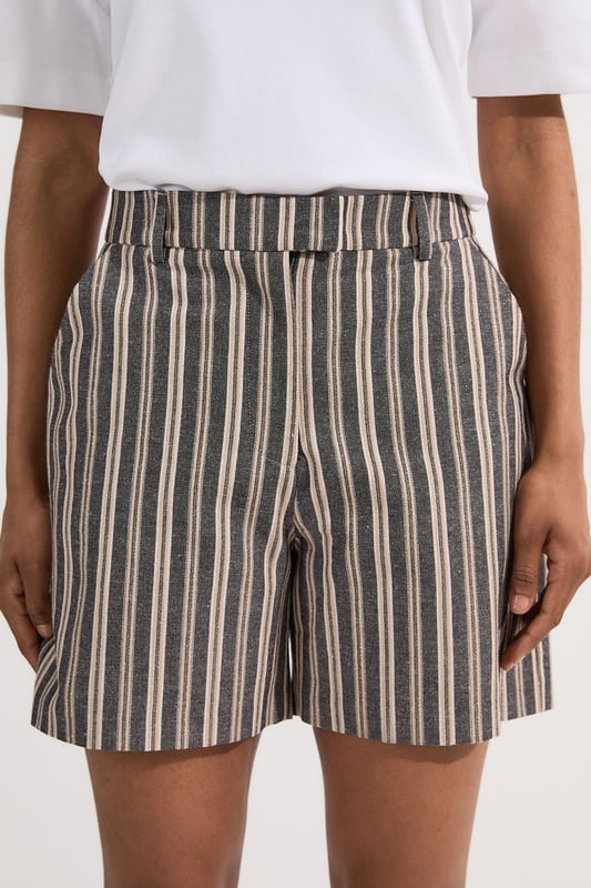 These Karen Millen tailored city shorts combine sophistication with casual comfort for effortless daywear styling. The distinctive stripe pattern with subtle sparkle threads creates visual interest while maintaining versatility. Style them with a crisp white t-shirt and an oversized blazer for a polished weekend brunch look, or pair with a lightweight knit and trainers for shopping trips and casual gatherings. The structured silhouette and linen blend fabric make these shorts perfect for warm-weather socialising without compromising on style. For a coordinated summer ensemble, match with flat sandals and a crossbody bag, adding sunglasses for a touch of chic practicality. These shorts transition seamlessly from daytime family gatherings to early evening garden parties, offering both comfort and refined style.  Tailored city shorts featuring a distinctive sparkle stripe pattern for a touch of subtle glamour Crafted with linen blend fabric for breathable comfort during warm weather Elegant gold-tone buckle detail at the waistband adds a refined finishing touch Practical side pockets for convenient storage of small essentials Versatile 45cm length offering a flattering fit that pairs beautifully with various tops  Matching piece available, sold separately.