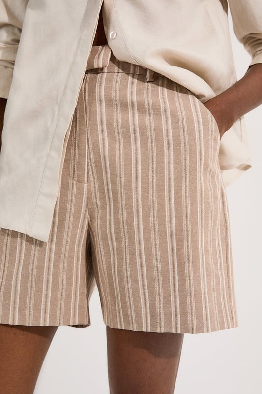 These Karen Millen tailored city shorts combine sophistication with casual comfort for effortless daywear styling. The distinctive stripe pattern with subtle sparkle threads creates visual interest while maintaining versatility. Style them with a crisp white t-shirt and an oversized blazer for a polished weekend brunch look, or pair with a lightweight knit and trainers for shopping trips and casual gatherings. The structured silhouette and linen blend fabric make these shorts perfect for warm-weather socialising without compromising on style. For a coordinated summer ensemble, match with flat sandals and a crossbody bag, adding sunglasses for a touch of chic practicality. These shorts transition seamlessly from daytime family gatherings to early evening garden parties, offering both comfort and refined style.  Tailored city shorts featuring a distinctive sparkle stripe pattern for a touch of subtle glamour Crafted with linen blend fabric for breathable comfort during warm weather Elegant gold-tone buckle detail at the waistband adds a refined finishing touch Practical side pockets for convenient storage of small essentials Versatile 45cm length offering a flattering fit that pairs beautifully with various tops  Matching piece available, sold separately.