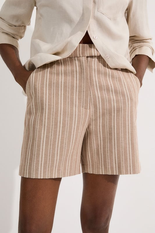 These Karen Millen tailored city shorts combine sophistication with casual comfort for effortless daywear styling. The distinctive stripe pattern with subtle sparkle threads creates visual interest while maintaining versatility. Style them with a crisp white t-shirt and an oversized blazer for a polished weekend brunch look, or pair with a lightweight knit and trainers for shopping trips and casual gatherings. The structured silhouette and linen blend fabric make these shorts perfect for warm-weather socialising without compromising on style. For a coordinated summer ensemble, match with flat sandals and a crossbody bag, adding sunglasses for a touch of chic practicality. These shorts transition seamlessly from daytime family gatherings to early evening garden parties, offering both comfort and refined style.  Tailored city shorts featuring a distinctive sparkle stripe pattern for a touch of subtle glamour Crafted with linen blend fabric for breathable comfort during warm weather Elegant gold-tone buckle detail at the waistband adds a refined finishing touch Practical side pockets for convenient storage of small essentials Versatile 45cm length offering a flattering fit that pairs beautifully with various tops  Matching piece available, sold separately.