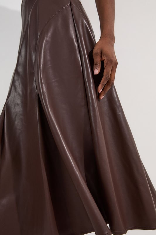 This Karen Millen faux leather midi skirt combines timeless elegance with contemporary edge. The full silhouette creates a dramatic swish with every step, while the high waistline accentuates your natural curves. Style with a fitted top for a balanced silhouette that highlights the skirt's voluminous design. For casual gatherings, pair it with a simple knit jumper and ankle boots, or dress it up with a crisp blouse and block heels for dinner dates. The versatile midi length works with both flats and heels, making this piece adaptable for family gatherings or weekend brunches. Add a cropped jacket and statement jewellery to transform this skirt into an ensemble that transitions effortlessly from day to evening wear.  Faux leather midi skirt with a full, flowing silhouette High-waisted design Elegant pleating detail Midi length Smooth finish with a subtle sheen