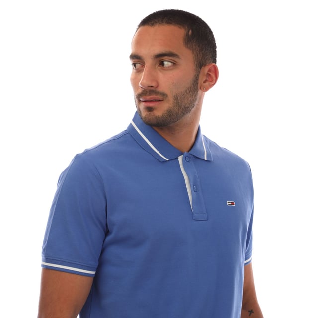 Mens Tommy Jeans Regular Fit Tipped Polo Shirt in blue.- Ribbed polo collar.- Two button placket.- Short sleeves with ribbed cuffs.- Contrast tipping at collar and cuffs- Embroidered Tommy Jeans flag patch at left chest.- Even vented hem.- Soft and comfortable cotton piqué fabric  made with at least 95% regenerative cotton.- Regular fit.- 100% Cotton.  Machine washable.- Ref: DM0DM20745C6E