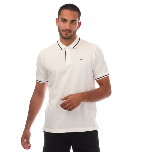 Mens Tommy Jeans Regular Fit Tipped Polo Shirt in white.- Ribbed polo collar.- Two button placket.- Short sleeves with ribbed cuffs.- Contrast tipping at collar and cuffs- Embroidered Tommy Jeans flag patch at left chest.- Even vented hem.- Soft and comfortable cotton piqué fabric  made with at least 95% regenerative cotton.- Regular fit.- 100% Cotton.  Machine washable.- Ref: DM0DM20745YBL
