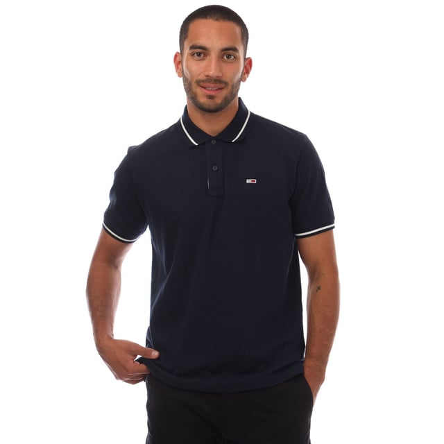 Mens Tommy Jeans Regular Fit Tipped Polo Shirt in navy.- Ribbed polo collar.- Two button placket.- Short sleeves with ribbed cuffs.- Contrast tipping at collar and cuffs- Embroidered Tommy Jeans flag patch at left chest.- Even vented hem.- Soft and comfortable cotton piqué fabric  made with at least 95% regenerative cotton.- Regular fit.- 100% Cotton.  Machine washable.- Ref: DM0DM20745C1G