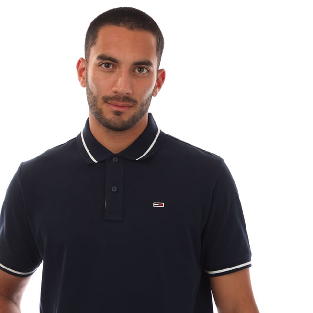 Mens Tommy Jeans Regular Fit Tipped Polo Shirt in navy.- Ribbed polo collar.- Two button placket.- Short sleeves with ribbed cuffs.- Contrast tipping at collar and cuffs- Embroidered Tommy Jeans flag patch at left chest.- Even vented hem.- Soft and comfortable cotton piqué fabric  made with at least 95% regenerative cotton.- Regular fit.- 100% Cotton.  Machine washable.- Ref: DM0DM20745C1G