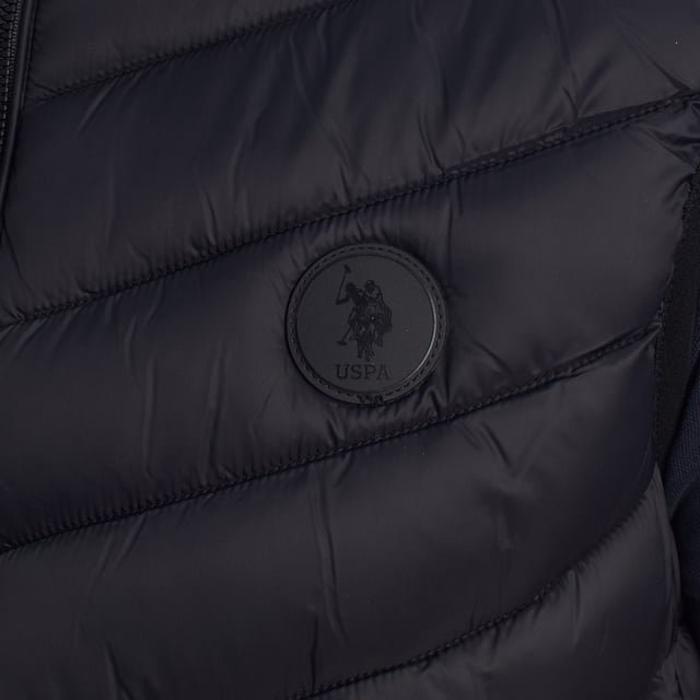 Diese Steppweste von US Polo Assn. wurde entwickelt, um Komfort und Schutz zu bieten, ohne auf Stil zu verzichten. vereint Leichtigkeit, Wärme und sportliche Eleganz. Seine gesteppte Konstruktion bietet eine ideale Wärmeisolierung für Übergangstage, während sein klares, zeitloses Design es zu einem vielseitigen Kleidungsstück für jeden Anlass macht.

 Details:
 - Normaler Schnitt mit hohem Halsausschnitt für mehr Schutz.
 - Frontverschluss mit hochwertigem, strapazierfähigem Reißverschluss.
 - Leichte Polsterung speichert die Wärme, ohne aufzutragen.
 - US Polo Assn. Auf der Brust eingeprägtes Logo, ein Symbol für Authentizität und Tradition.
 - Funktionelles Design, ideal zum alleinigen Tragen oder als zusätzliche Schicht.

 Seit 1890 in der US Polo Assn. Wir entwerfen Kleidungsstücke, die von den Werten des Polosports inspiriert sind: Eleganz, Leistung und Authentizität. Diese Weste ist ein Ausdruck dieses Erbes und wurde für den modernen Mann entworfen, der dynamisch und stilvoll lebt.
 Komposition: 100 % recyceltes Polyamid
 Pflege:
Handwäsche.
 Verwenden Sie kein Bleichmittel.
 Nicht im Trockner trocknen.
 Kein Bügeln.