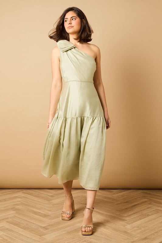 Striking one-shoulder design with an elegant oversized bow detail
        Feminine midi length with a flattering tiered skirt
        Lightweight Tencel fabric that drapes beautifully
        Clean, minimalist silhouette perfect for special occasions
        Versatile design that can be dressed up or down with accessories
    
    This enchanting one-shoulder midi dress showcases Oasis's signature feminine aesthetic with its standout bow shoulder detail. The graceful tiered skirt creates movement and dimension whilst maintaining a sophisticated silhouette. Style with strappy heeled sandals and statement earrings for summer weddings or garden parties. For race day events, pair with a fascinator and clutch bag for a refined ensemble. The versatile design transitions beautifully from daytime celebrations to evening soires-simply switch your accessories to match the occasion. The clean lines and classic shape make this dress a timeless addition to your occasion wardrobe, whilst the midi length offers both elegance and practicality. Perfect for those moments when you want to make a subtle yet memorable impression.