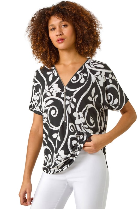 Textured Print Zip Detail Top from Roman. Stand out this Spring/Summer in this textured print top adorned with an all over abstract floral leaf print. Crafted from a stylish ITY puff print fabric, this top features a unique zip neck detail that adds an edgy touch. The short sleeves and rounded hemline create a flattering silhouette that pairs perfectly with jeans and sandals for a casual yet fashionable look.