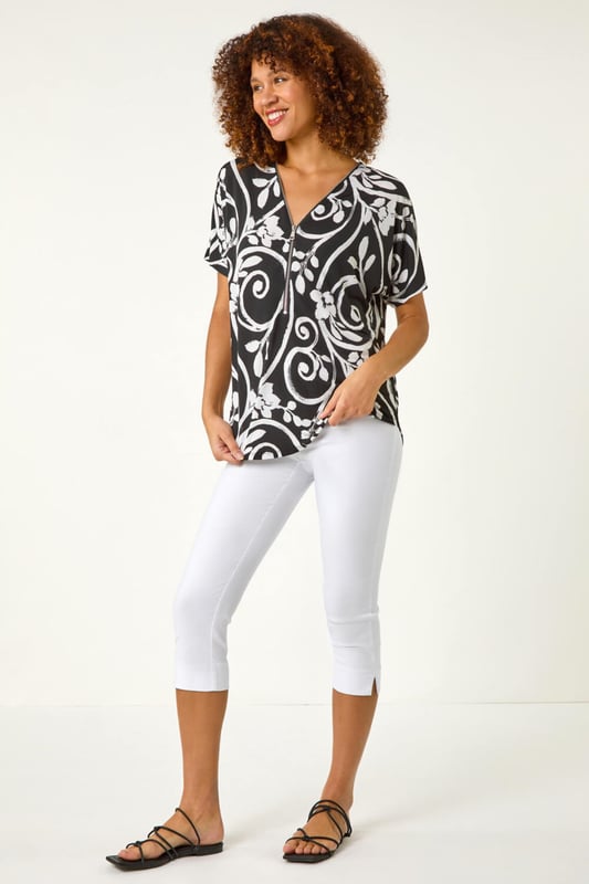 Textured Print Zip Detail Top from Roman. Stand out this Spring/Summer in this textured print top adorned with an all over abstract floral leaf print. Crafted from a stylish ITY puff print fabric, this top features a unique zip neck detail that adds an edgy touch. The short sleeves and rounded hemline create a flattering silhouette that pairs perfectly with jeans and sandals for a casual yet fashionable look.