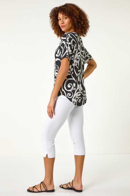 Textured Print Zip Detail Top from Roman. Stand out this Spring/Summer in this textured print top adorned with an all over abstract floral leaf print. Crafted from a stylish ITY puff print fabric, this top features a unique zip neck detail that adds an edgy touch. The short sleeves and rounded hemline create a flattering silhouette that pairs perfectly with jeans and sandals for a casual yet fashionable look.