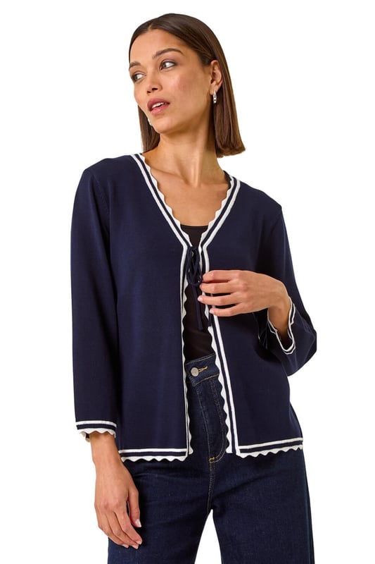 Scallop Edge Tie Cardigan from Roman. Add a touch of elegance to your Autumn/Winter wardrobe with this charming scallop edge cardigan. This lightweight piece features a unique contrast knit detail and is designed in an edge to edge style with a tie detail and delicate scallop edge. Perfect for layering, this versatile piece pairs beautifully with a simple t-shirt and jeans for a chic and polished look.