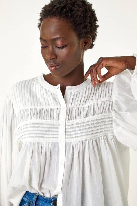 Pleat Detail Button Through Blouse from Roman. Add a touch of sophistication to your wardrobe with this pleat detail button-through blouse. Crafted from a soft cotton fabric, this classic round neckline design features long sleeves to keep you warm during the Autumn Winter. Complete with stylish front pleat detail and trendy button-through opening, this blouse adds a subtle elegance to your outfit. Style effortlessly with jeggings and ankle boots for a complete fall look!