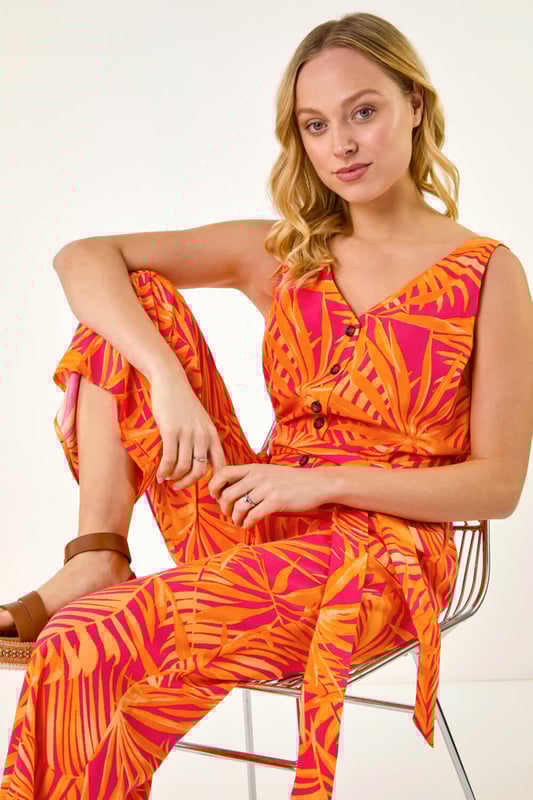 Dusk Palm Print Belted Jumpsuit from Roman. Get ready to make a statement in this chic palm print jumpsuit for the upcoming Spring/Summer season. Featuring a flattering v-neck and sleeveless design, this woven jumpsuit is perfect for sunny days. The belted waist detail adds a touch of elegance and ensures a great fit. Complete your look with sandals and a trendy denim jacket for effortless style!