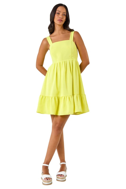 Dusk Poplin Tiered Swing Dress from Roman. Unleash your inner fashionista with this trendy tiered swing dress, perfect for the Spring Summer season. Crafted from a soft poplin woven fabric, this knee length beauty features a classic square neckline and sleeveless style. The swing shape and tiered skirt add a touch of fun to your outfit, ensuring you stand out in style. Pair with a cardigan and wedge heels for a complete look!