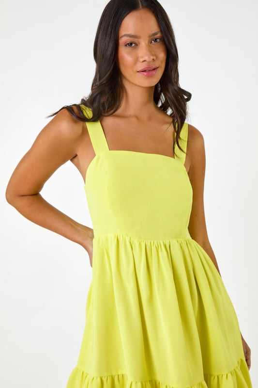 Dusk Poplin Tiered Swing Dress from Roman. Unleash your inner fashionista with this trendy tiered swing dress, perfect for the Spring Summer season. Crafted from a soft poplin woven fabric, this knee length beauty features a classic square neckline and sleeveless style. The swing shape and tiered skirt add a touch of fun to your outfit, ensuring you stand out in style. Pair with a cardigan and wedge heels for a complete look!