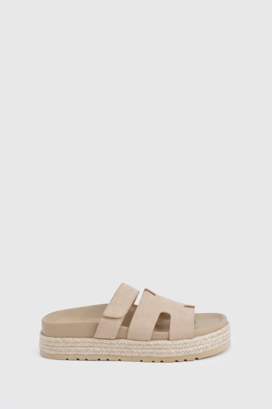 Faux suede slides with distinctive cut-out strap design for breathability
        Flatform espadrille-style sole with textured detailing for added grip
        Flat heel height (0-2cm) offering all-day comfort without sacrificing style
        Cushioned footbed providing essential support for extended wear
        Adjustable strap with buckle fastening for a customisable fit
    
    These versatile slides combine casual charm with practical design, perfect for effortless summer styling. The flatform espadrille-inspired sole adds subtle height whilst maintaining walkability, making them ideal for everything from beach days to city strolls. Pair with frayed denim shorts and an oversized linen shirt for a relaxed daytime look, or style with a flowing maxi dress for casual garden parties. The neutral finish ensures these slides will complement virtually any outfit in your warm-weather wardrobe. Their cushioned construction means you can comfortably wear them all day, whether you're running errands or meeting friends for brunch. A true summer essential that balances fashion-forward design with everyday functionality - the ultimate footwear solution for the girl who values both style and comfort.