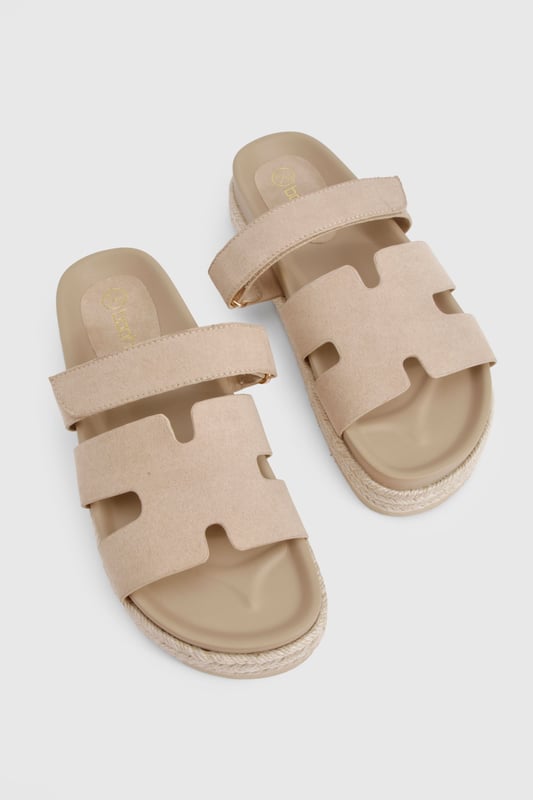 Faux suede slides with distinctive cut-out strap design for breathability
        Flatform espadrille-style sole with textured detailing for added grip
        Flat heel height (0-2cm) offering all-day comfort without sacrificing style
        Cushioned footbed providing essential support for extended wear
        Adjustable strap with buckle fastening for a customisable fit
    
    These versatile slides combine casual charm with practical design, perfect for effortless summer styling. The flatform espadrille-inspired sole adds subtle height whilst maintaining walkability, making them ideal for everything from beach days to city strolls. Pair with frayed denim shorts and an oversized linen shirt for a relaxed daytime look, or style with a flowing maxi dress for casual garden parties. The neutral finish ensures these slides will complement virtually any outfit in your warm-weather wardrobe. Their cushioned construction means you can comfortably wear them all day, whether you're running errands or meeting friends for brunch. A true summer essential that balances fashion-forward design with everyday functionality - the ultimate footwear solution for the girl who values both style and comfort.