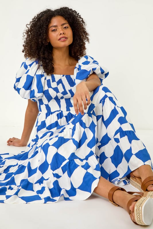 Dusk Geo Print Tiered Dress from Roman. Feel effortless this Spring Summer season with our Dusk tiered geo print dress. This trendy dress features a square neckline and playful short puff sleeves, adding a fun touch to your outfit. Cut and lined with a comfortable woven fabric, the dress boasts a flattering shirred bodice and a midi length tiered skirt, ensuring all-day comfort. Style with a denim jacket and wedge heels for the perfect look you'll love!