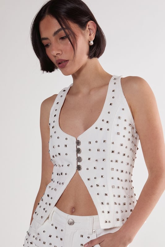 Striking studded embellishment across the denim fabric for a bold statement look
        Flattering V neckline with button-through front design
        Structured corset silhouette that accentuates the waistline
        Sleeveless design with wide straps for comfortable support
        Versatile denim construction that pairs perfectly with the matching shorts or other separates
    
    Make a striking impression with this Nasty Gal Studded Denim Corset Top, designed to command attention on your next night out. The all-over stud detailing transforms classic denim into a head-turning piece that captures the light as you move. Style with the coordinating denim shorts as seen on our model for a contemporary co-ord look, or mix with high-waisted trousers for a contrasting silhouette. For an edgy evening ensemble, pair with leather trousers and chunky boots, or soften the look with a flowing midi skirt. This versatile piece transitions effortlessly from casual drinks to club nights-simply adjust your accessories to suit the occasion. The structured corset design flatters your figure while the cotton fabric ensures comfort throughout your night on the town.