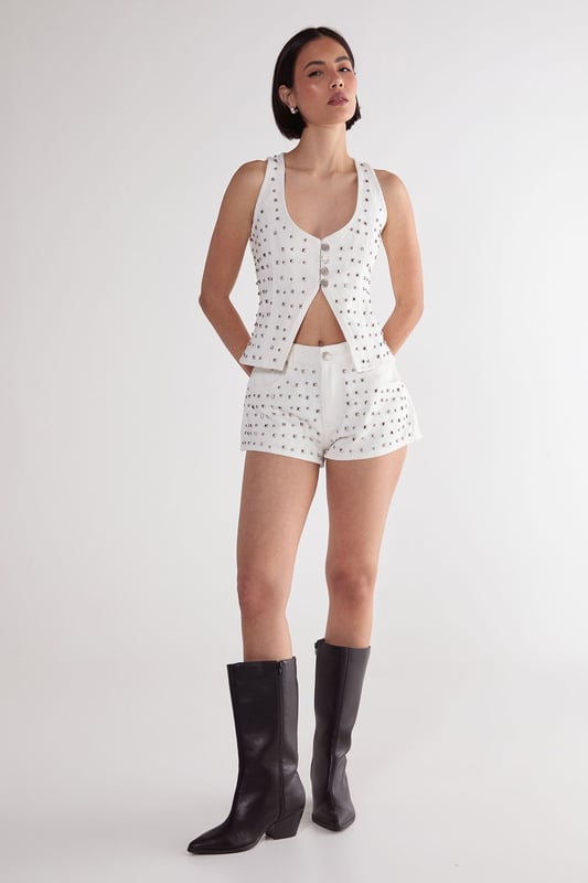 Striking studded embellishment across the denim fabric for a bold statement look
        Flattering V neckline with button-through front design
        Structured corset silhouette that accentuates the waistline
        Sleeveless design with wide straps for comfortable support
        Versatile denim construction that pairs perfectly with the matching shorts or other separates
    
    Make a striking impression with this Nasty Gal Studded Denim Corset Top, designed to command attention on your next night out. The all-over stud detailing transforms classic denim into a head-turning piece that captures the light as you move. Style with the coordinating denim shorts as seen on our model for a contemporary co-ord look, or mix with high-waisted trousers for a contrasting silhouette. For an edgy evening ensemble, pair with leather trousers and chunky boots, or soften the look with a flowing midi skirt. This versatile piece transitions effortlessly from casual drinks to club nights-simply adjust your accessories to suit the occasion. The structured corset design flatters your figure while the cotton fabric ensures comfort throughout your night on the town.