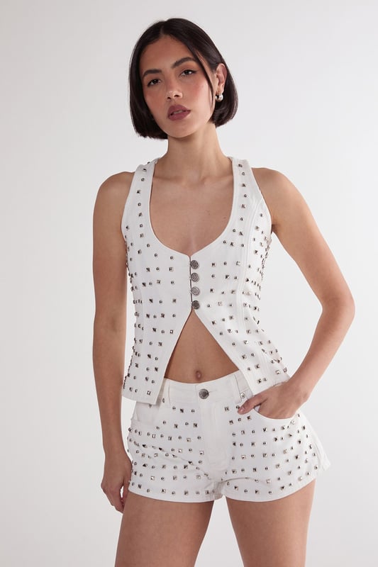 Striking studded embellishment across the denim fabric for a bold statement look
        Flattering V neckline with button-through front design
        Structured corset silhouette that accentuates the waistline
        Sleeveless design with wide straps for comfortable support
        Versatile denim construction that pairs perfectly with the matching shorts or other separates
    
    Make a striking impression with this Nasty Gal Studded Denim Corset Top, designed to command attention on your next night out. The all-over stud detailing transforms classic denim into a head-turning piece that captures the light as you move. Style with the coordinating denim shorts as seen on our model for a contemporary co-ord look, or mix with high-waisted trousers for a contrasting silhouette. For an edgy evening ensemble, pair with leather trousers and chunky boots, or soften the look with a flowing midi skirt. This versatile piece transitions effortlessly from casual drinks to club nights-simply adjust your accessories to suit the occasion. The structured corset design flatters your figure while the cotton fabric ensures comfort throughout your night on the town.