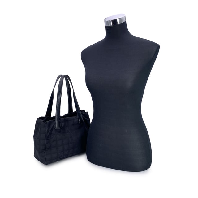 VINTAGE, RRP AS NEW
Chanel Travel Line Tote (2003-2004) - Understated Elegance in Motion  Timeless, functional, and distinctly Chanel - this black jacquard nylon tote from the house's Travel Line collection is a minimalist masterpiece from the 2003-2004 era, designed with the modern voyager in mind.  Crafted from sleek black jacquard nylon, the bag features the iconic Chanel motif subtly woven into the fabric - a quiet nod to the maison's storied heritage. The silhouette is elevated by a black leather shoulder straps/handles, offering both comfort and sophistication for life on the move.  Inside, the nylon lining holds two side zip pockets, perfect for keeping essentials within reach while maintaining the tote's clean lines. True to Chanel's legacy of craftsmanship, the interior bears the 'Chanel - Made in Italy' tag and a discreet ity hologram, grounding this vintage gem in ity and history.  Effortlessly chic and endlessly versatile, this Chanel Travel Line tote is a sophisticated companion - ideal for everyday elegance, city strolls, or quiet getaways. A rare find for collectors and lovers of early-2000s Chanel. Condition Rating: B - VERY GOOD CONDITIONCondition Details: Some wear of use on bottom corners. Some normal wear of use on leather handles. Please, look carefully at the photos and ask if you have any doubts.Measurements (cm):Depth: 11.4Height: 20.3Length: 27.9Other Details: Dustbag? NoKeys? NoBox? No Measurments:  width: 114 mm length: 279 mm height: 203 mm
